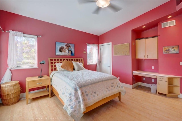 bedroom featuring built in desk, lofted ceiling, ceiling fan, light hardwood / wood-style flooring, and a closet