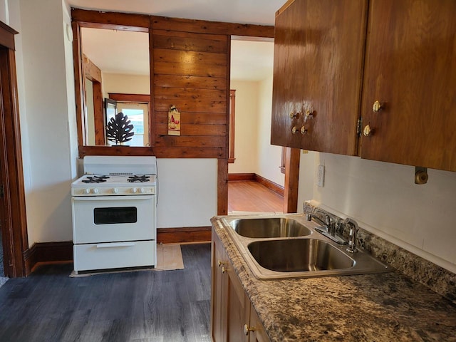 kitchen with sink, dark wood-type flooring, dark stone countertops, and white gas stove