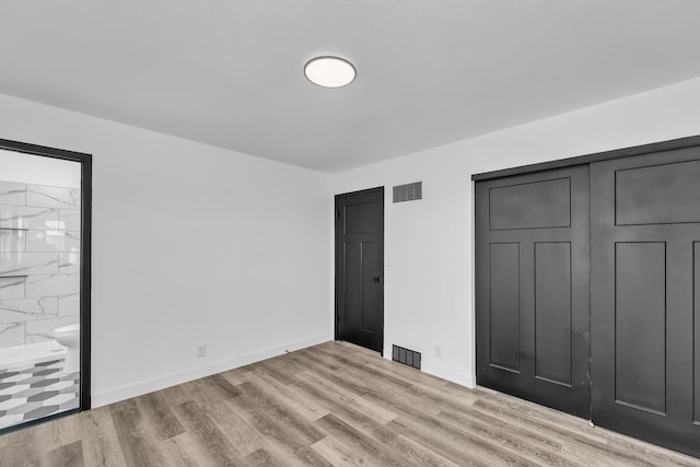 unfurnished bedroom featuring light hardwood / wood-style floors, ensuite bathroom, and a closet