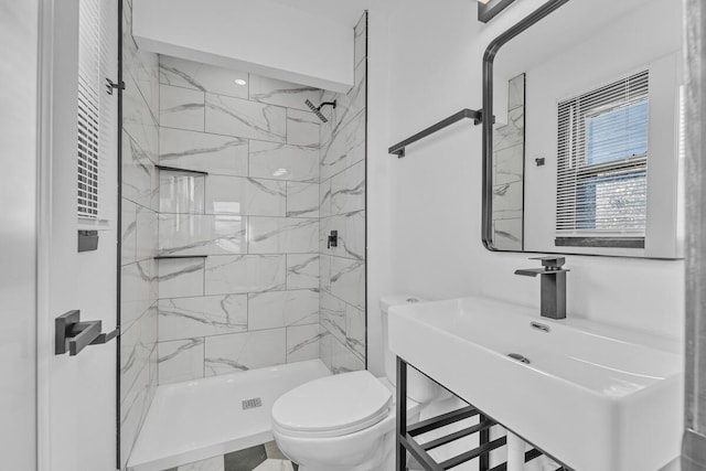 bathroom featuring toilet, a tile shower, and sink