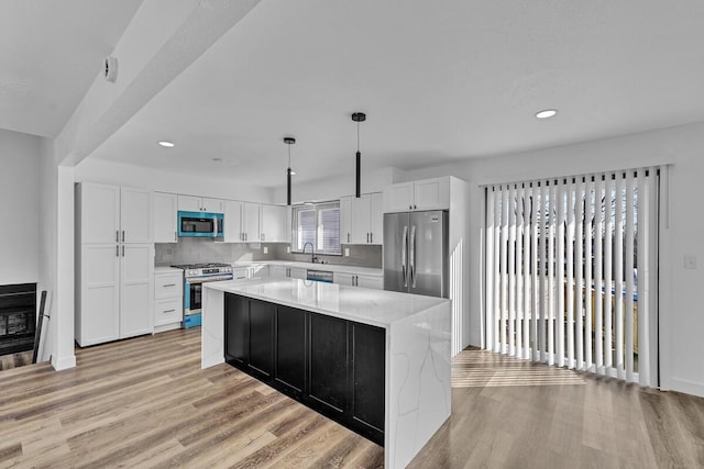 kitchen with pendant lighting, stainless steel appliances, a kitchen island, white cabinetry, and sink