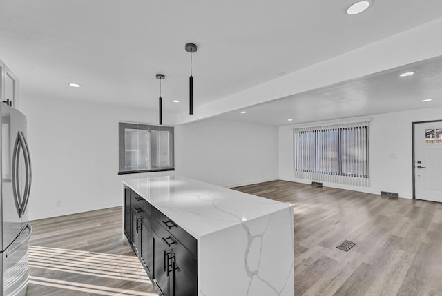 kitchen featuring a kitchen island, stainless steel refrigerator, light hardwood / wood-style flooring, hanging light fixtures, and light stone countertops