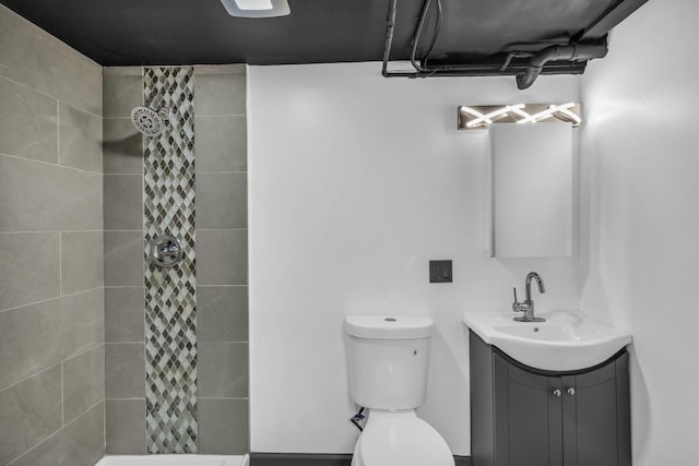 bathroom with toilet, a tile shower, and vanity