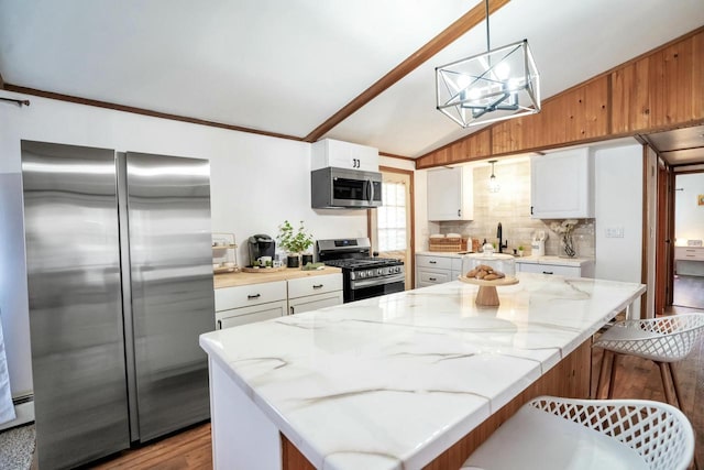 kitchen featuring stainless steel appliances, white cabinets, decorative light fixtures, lofted ceiling, and a chandelier