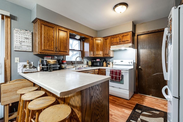 kitchen with white appliances, kitchen peninsula, light hardwood / wood-style floors, a breakfast bar area, and sink