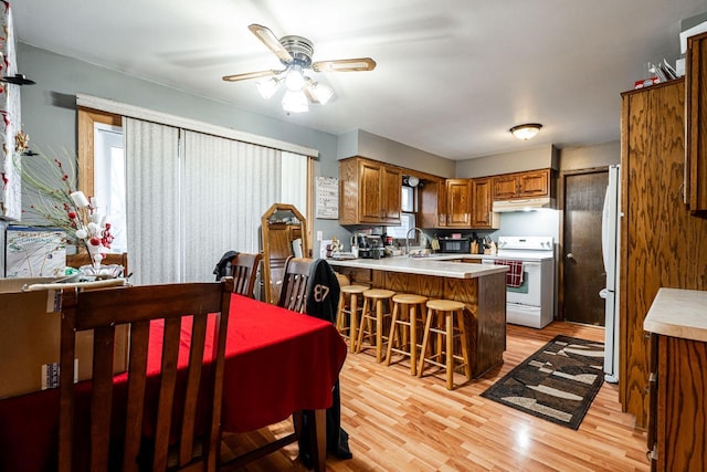 kitchen with white appliances, a kitchen bar, light wood-type flooring, kitchen peninsula, and a wealth of natural light