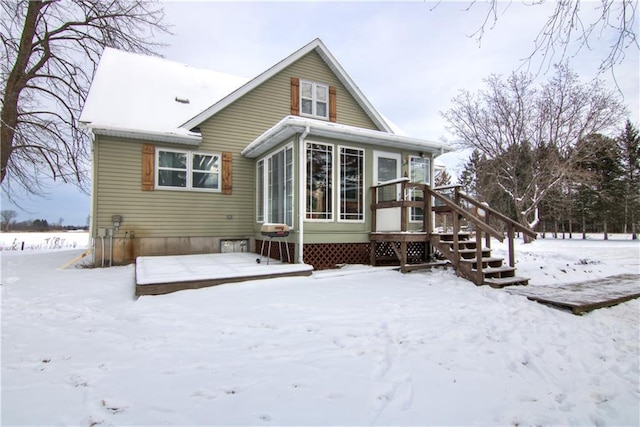 snow covered rear of property with a sunroom