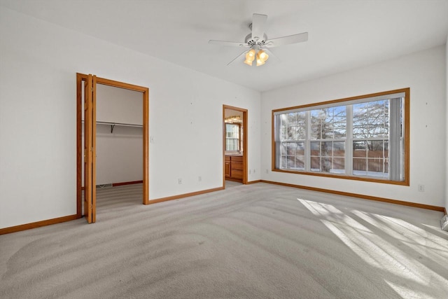 unfurnished bedroom featuring ceiling fan, light colored carpet, ensuite bath, a walk in closet, and a closet