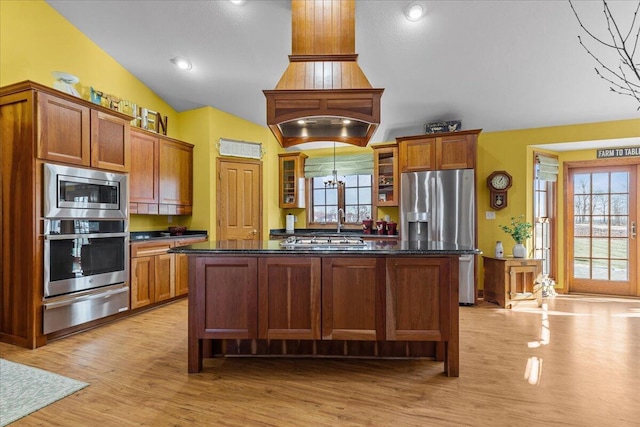 kitchen featuring vaulted ceiling, appliances with stainless steel finishes, a center island, and light hardwood / wood-style flooring