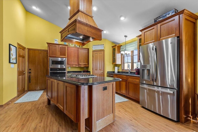 kitchen featuring a kitchen island, decorative light fixtures, stainless steel appliances, dark stone counters, and light wood-type flooring