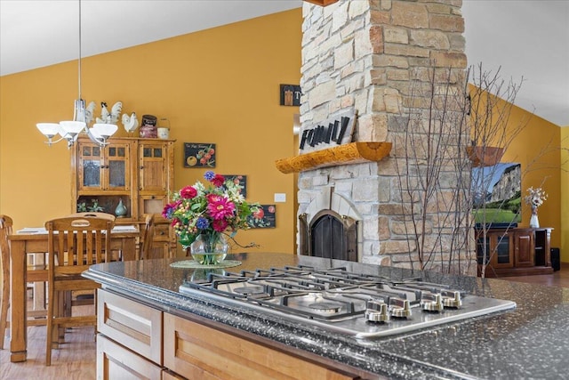 kitchen with decorative light fixtures, a notable chandelier, a fireplace, stainless steel gas cooktop, and light brown cabinetry