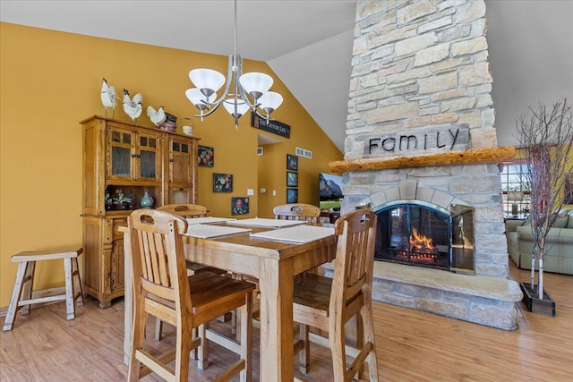 dining space featuring light hardwood / wood-style floors, a chandelier, high vaulted ceiling, and a stone fireplace