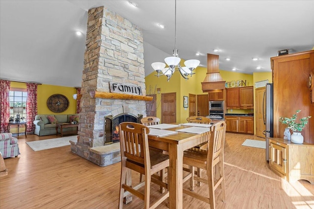 dining area featuring light hardwood / wood-style floors, high vaulted ceiling, a stone fireplace, and a notable chandelier