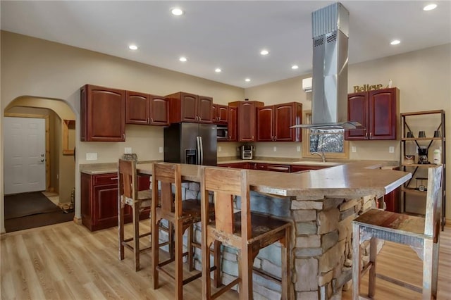 kitchen with light hardwood / wood-style floors, kitchen peninsula, island exhaust hood, appliances with stainless steel finishes, and a breakfast bar area