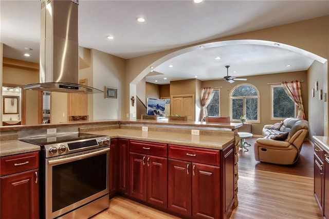 kitchen with stainless steel range with electric stovetop, ceiling fan, island range hood, and light hardwood / wood-style flooring