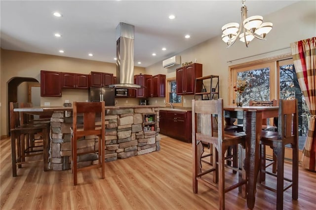 kitchen with appliances with stainless steel finishes, a wall mounted air conditioner, light wood-type flooring, a notable chandelier, and hanging light fixtures