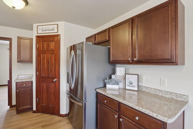 kitchen with light stone counters, stainless steel fridge with ice dispenser, and light hardwood / wood-style flooring