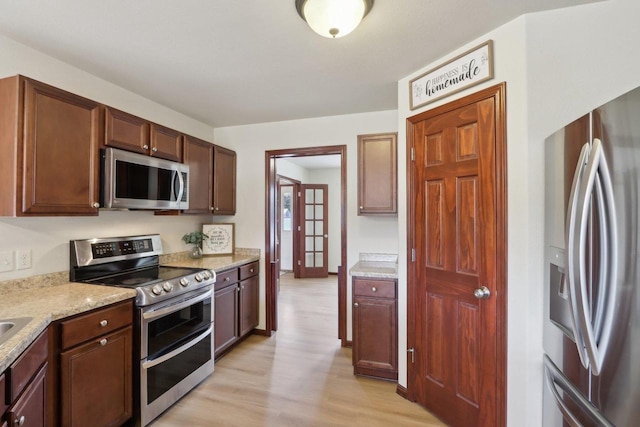 kitchen with light stone countertops, stainless steel appliances, and light hardwood / wood-style flooring