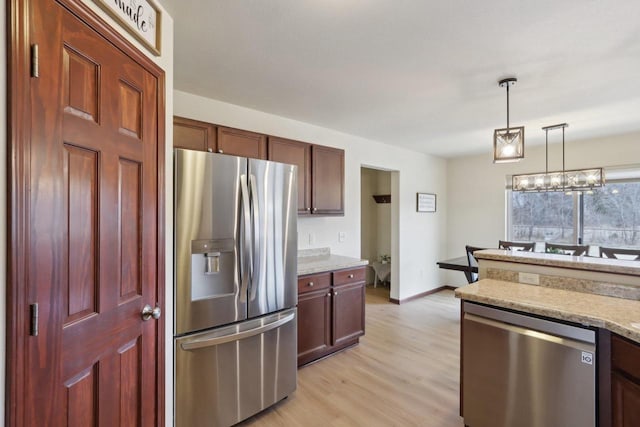 kitchen featuring light hardwood / wood-style floors, appliances with stainless steel finishes, hanging light fixtures, a chandelier, and light stone counters