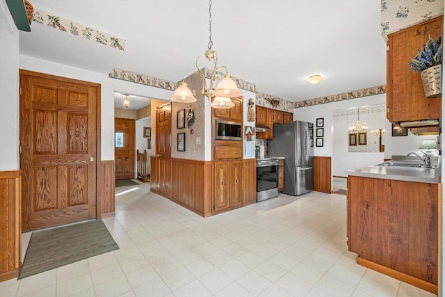 kitchen with sink, wooden walls, hanging light fixtures, appliances with stainless steel finishes, and a chandelier