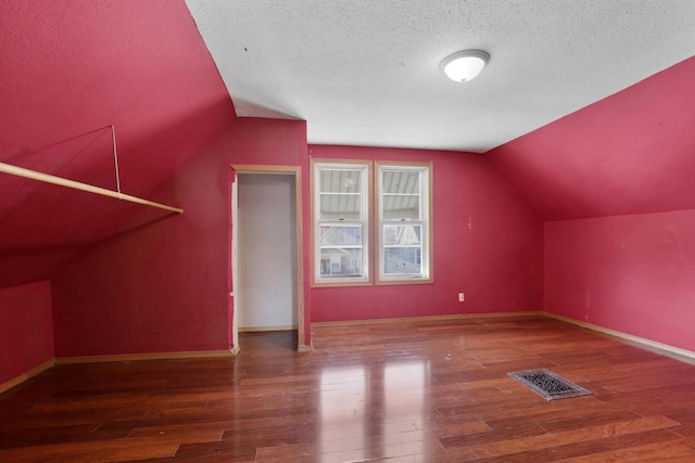 additional living space featuring a textured ceiling, dark hardwood / wood-style floors, and vaulted ceiling