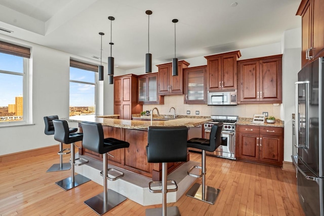 kitchen featuring premium appliances, decorative light fixtures, a kitchen bar, light stone counters, and a center island with sink