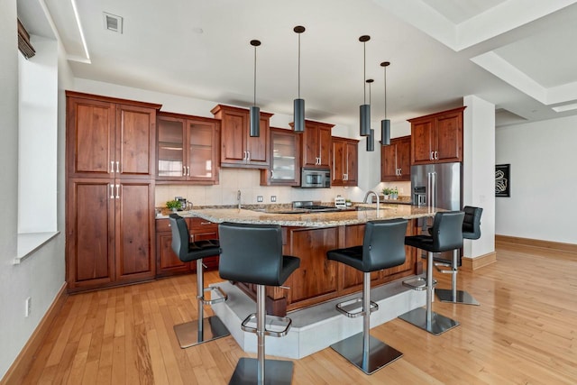 kitchen with hanging light fixtures, appliances with stainless steel finishes, light stone counters, and a center island with sink