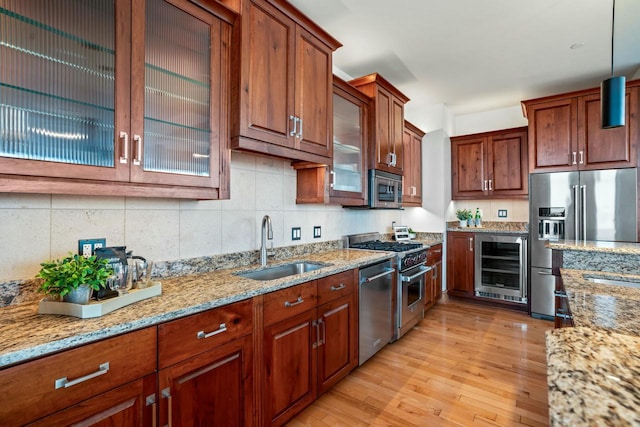 kitchen with light stone countertops, beverage cooler, sink, hanging light fixtures, and high quality appliances