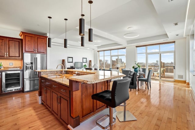 kitchen featuring an island with sink, high end fridge, beverage cooler, pendant lighting, and sink