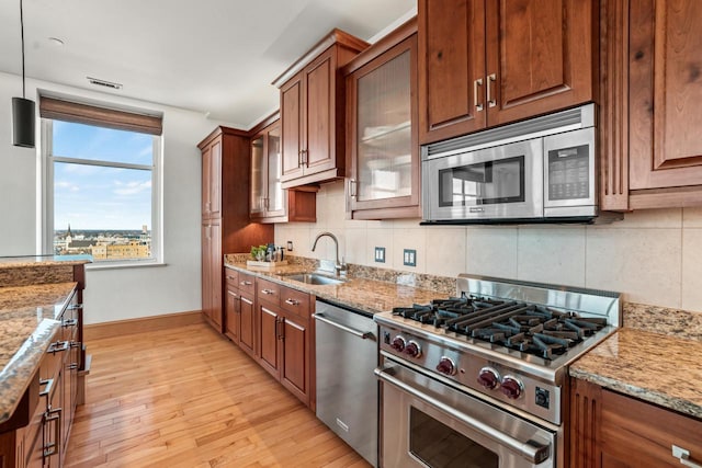 kitchen with sink, light stone counters, stainless steel appliances, and pendant lighting