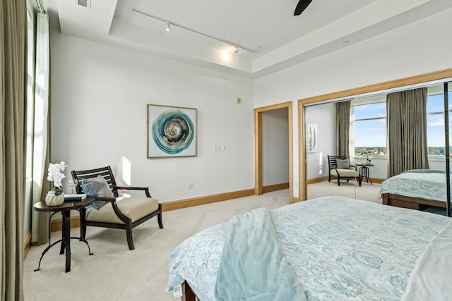 bedroom featuring ceiling fan, track lighting, light colored carpet, and a tray ceiling