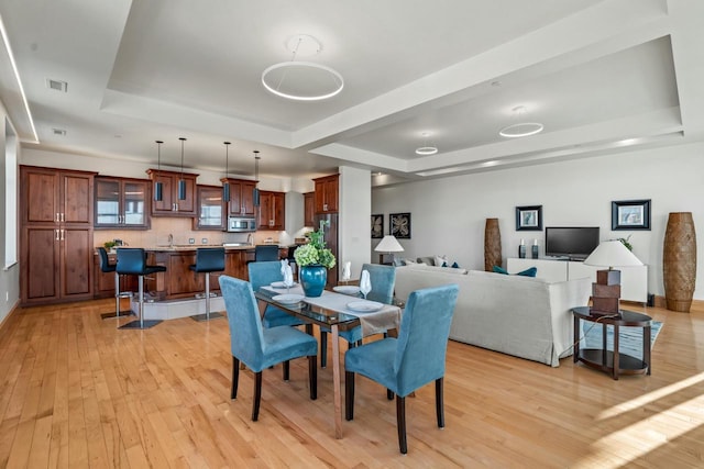 dining space with a raised ceiling, sink, and light hardwood / wood-style flooring