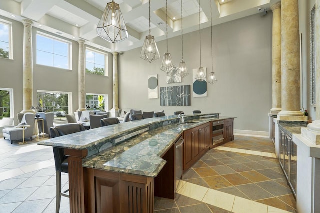 kitchen featuring hanging light fixtures, a kitchen breakfast bar, dark stone countertops, and ornate columns