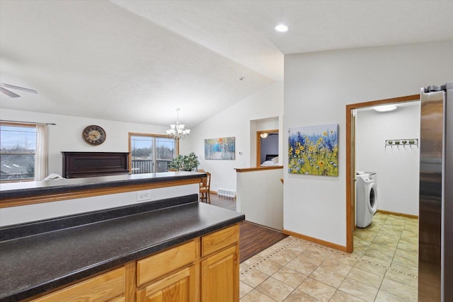 kitchen with ceiling fan with notable chandelier, washer and dryer, vaulted ceiling, hanging light fixtures, and stainless steel refrigerator