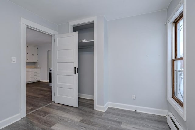 unfurnished bedroom with baseboard heating, a closet, and hardwood / wood-style flooring