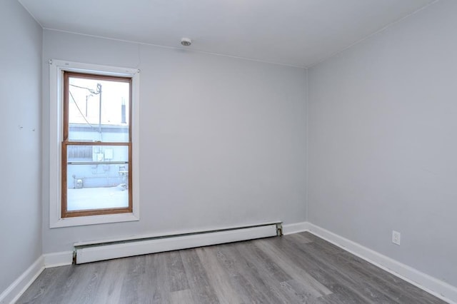 unfurnished room featuring hardwood / wood-style floors and a baseboard heating unit