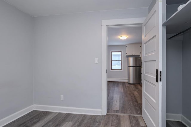 empty room featuring a baseboard heating unit and dark wood-type flooring