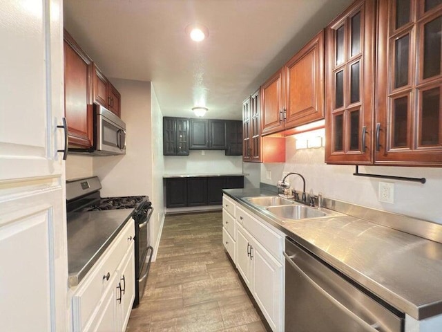 kitchen with appliances with stainless steel finishes, stainless steel counters, white cabinetry, wood-type flooring, and sink