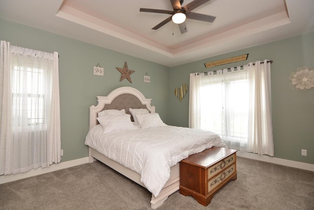 carpeted bedroom with ceiling fan and a tray ceiling