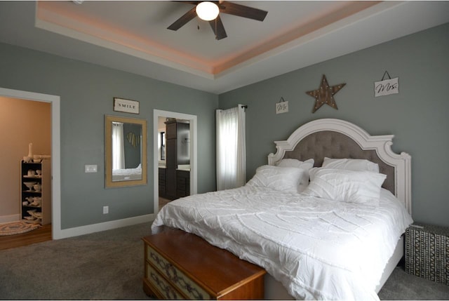 bedroom featuring ceiling fan, connected bathroom, a tray ceiling, and dark colored carpet