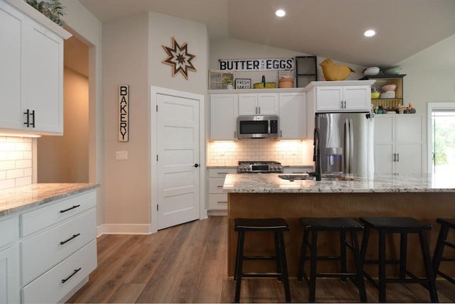 kitchen with appliances with stainless steel finishes, dark hardwood / wood-style flooring, vaulted ceiling, white cabinets, and light stone counters