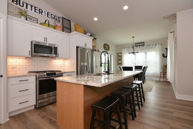 kitchen with white cabinetry, a kitchen bar, stainless steel appliances, and a center island with sink