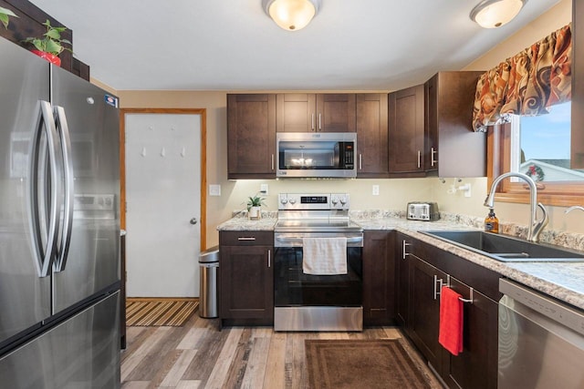 kitchen with dark brown cabinets, appliances with stainless steel finishes, sink, and light hardwood / wood-style floors