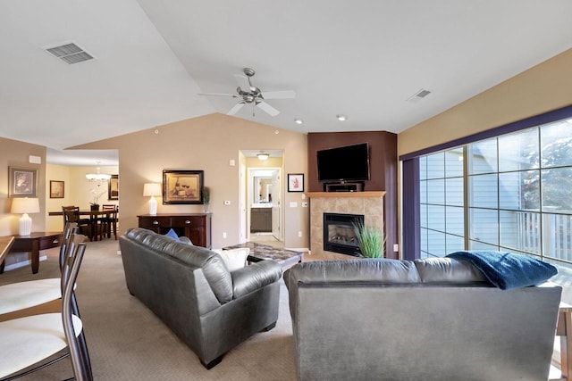 carpeted living room with vaulted ceiling, ceiling fan with notable chandelier, and a tiled fireplace