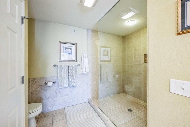 bathroom with tile walls, tile patterned floors, tiled shower, and toilet