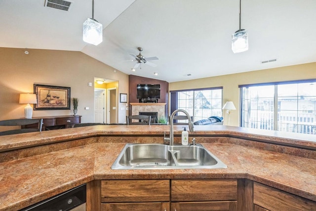 kitchen with a tiled fireplace, decorative light fixtures, lofted ceiling, stainless steel dishwasher, and sink