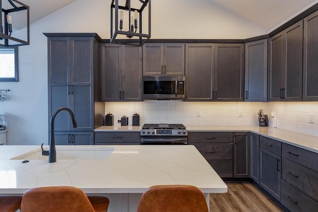 kitchen with stainless steel appliances, tasteful backsplash, a kitchen breakfast bar, hanging light fixtures, and vaulted ceiling