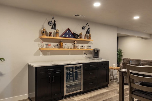 bar with wine cooler, light hardwood / wood-style flooring, and light stone countertops