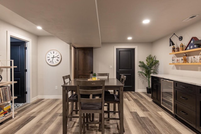 dining space featuring bar, wine cooler, and light hardwood / wood-style flooring