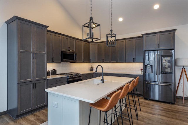 kitchen featuring appliances with stainless steel finishes, decorative light fixtures, tasteful backsplash, an island with sink, and sink